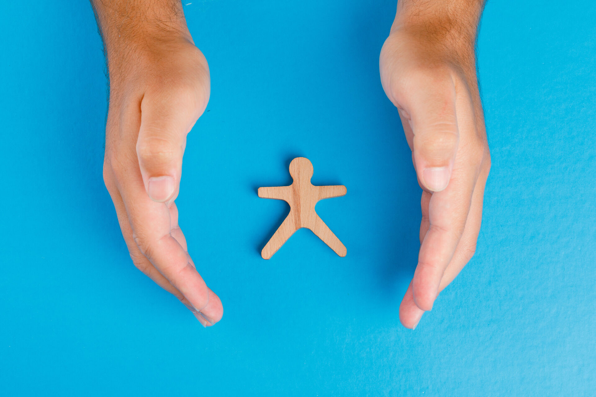 social-protection-concept-on-blue-table-flat-lay-hands-taking-care-of-wooden-human-figure